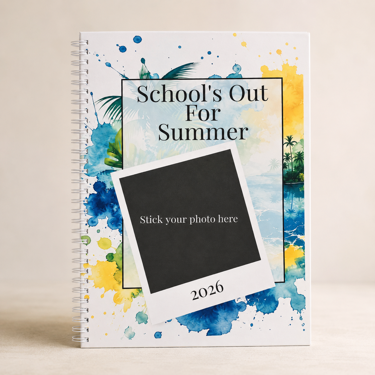 A spiral-bound notebook with a tropical watercolor cover design featuring blue splashes, palm leaves, and a sunset scene. The cover displays the text 'School's Out For Summer' and a large black-and-white placeholder card that says 'Stick your photo here' with '2026' at the bottom.